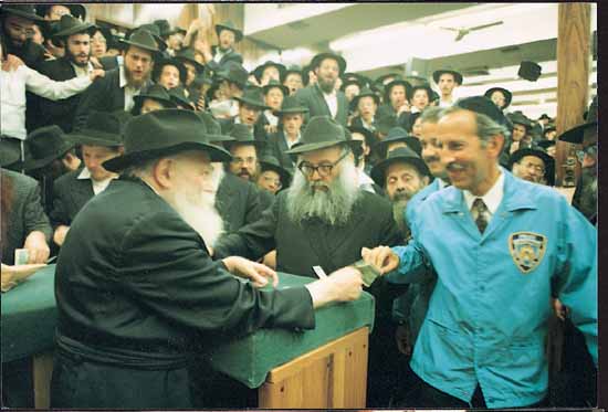 The Rebbe handing a dollar and a blessing to a visitor in a crowded hall